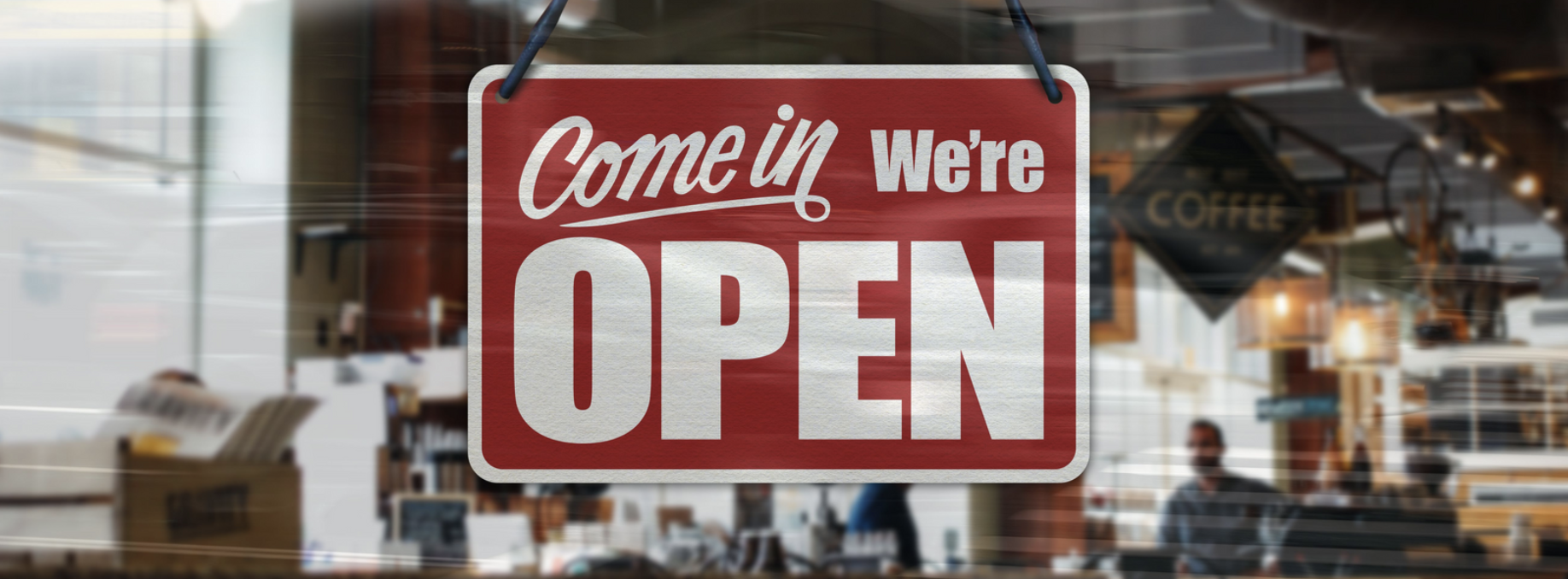 'Come in we're open' sign hanging in a shop window.